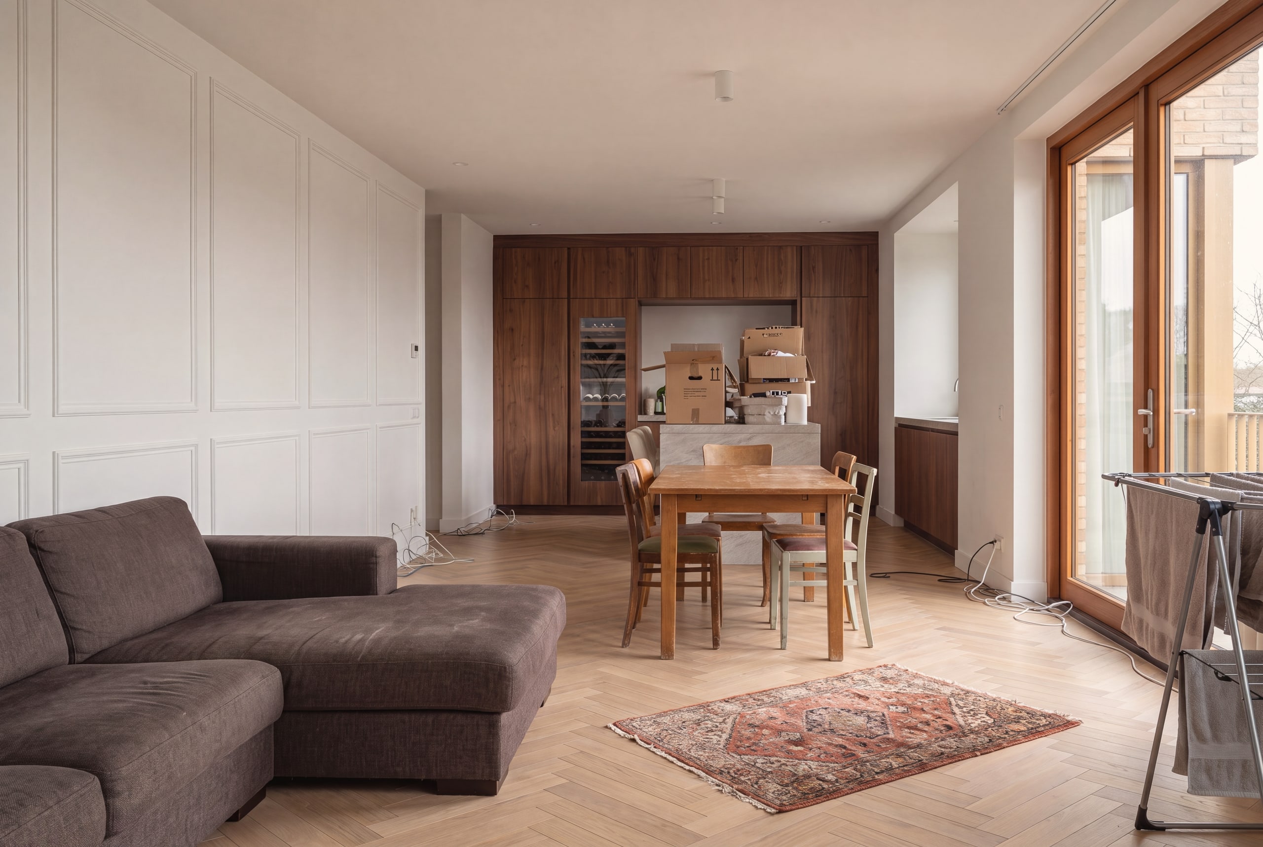 Dezelfde woonkamer vóór de styling: versleten bank, losse stoelen en verhuisdozen op het kookeiland